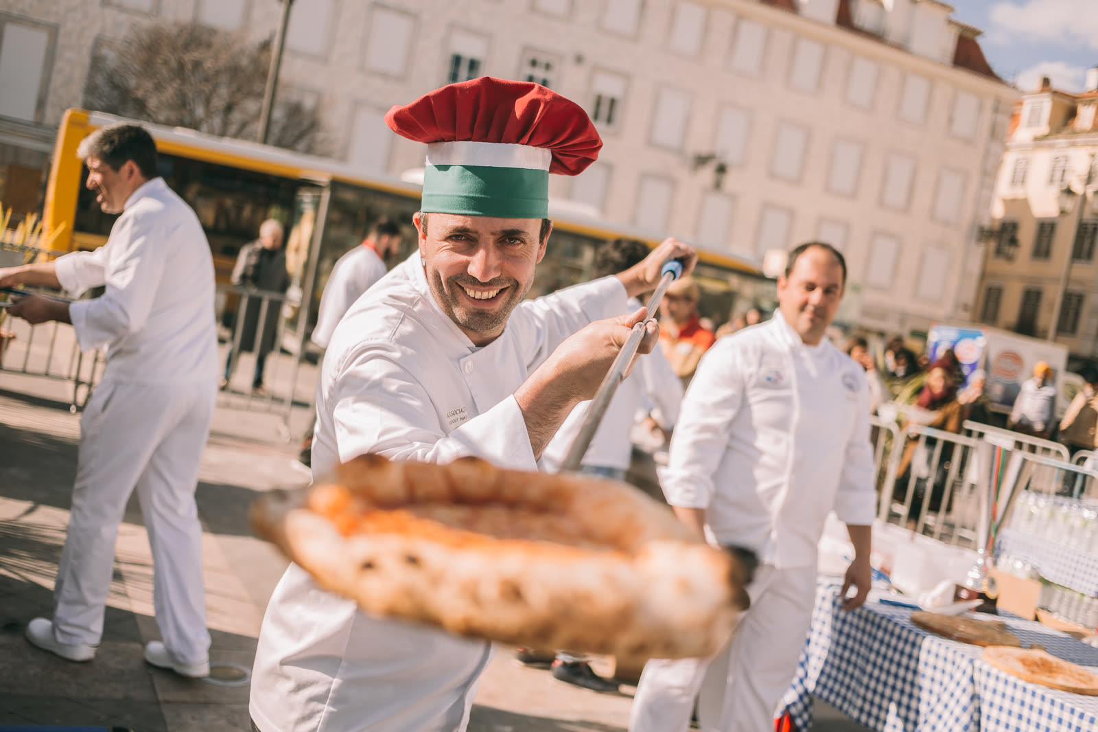 Pizzaiolo com chapéu tricolor tira uma pizza do forno no Dia Mundial do Pizzaiolo