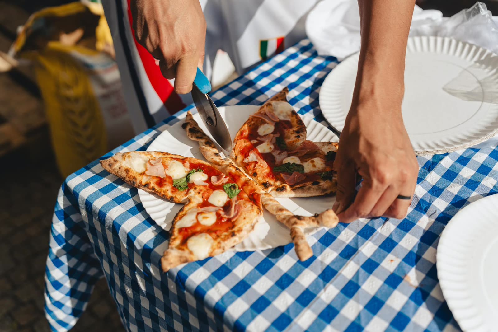 Mãos a cortar e partilhar uma pizza numa toalha aos quadrados